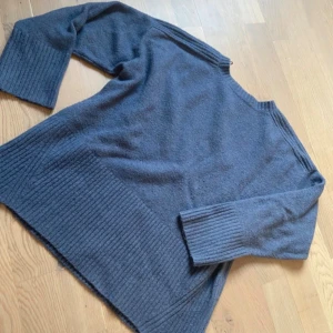 Mörkgrå stickad tröja från Zara - Mysig mörkgrå stickad tröja från Zara med bred ribbad kant nertill och vid ärmslut. Tröjan har en rak passform och trekvartsärmar, perfekt för lager-på-lager under kyliga dagar.