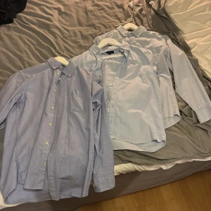 Tre ljusblå skjortor med krage - Säljer tre klassiska ljusblå skjortor med krage och knäppning framtill. Alla har lång ärm och bröstficka, perfekta för en clean och stilren look. Skjortorna är i bomull och har en normal passform. Alla är i Xs förutom gant i mitten som är 170cm!