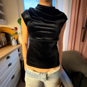 Svart sammets topp med hög krage - Snygg svart topp i mjuk sammet med hög krage och ärmlös design. Toppen har en figurnära passform och en stilren look som passar perfekt till jeans eller kjol. Materialet ger en lyxig känsla och den svarta färgen gör den lätt att matcha.😻😻 En riktig snygg festtopp😻