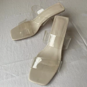 Beiga sandaler med transparent klack 38 - Säljer ett par trendiga sandaler från Pull&Bear med fyrkantig tå, transparenta remmar och cool genomskinlig klack. Enstaka sträck/märken på klacken förekommer men inget som syns i helheten bara om man kollar nära!