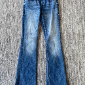Blå bootcut jeans från H&M, low waist - Snygga blå bootcut jeans från H&M med låg midja och justerbar midja. Klassisk femficksmodell med ljus tvätt och utsvängda ben. Materialet är en blandning av bomull och polyester med lite stretch för extra komfort. Mått Midjan: ca 36 cm Längd från grenen och ner: ca 82 cm  78% bomull, 20% polyester och 2% elastan  Kommer från ett djur och rökfritt hem.