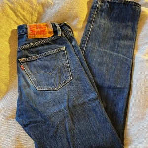 Levi's 501 blå jeans W30 L32 - Klassiska Levi's 501 jeans i blå denim med raka ben och normal passform. Snygga kontrastsömmar, fem fickor och ikonisk läderpatch bak i midjan. Perfekta för dig som gillar tidlös stil och vill ha ett par jeans som funkar till allt.
