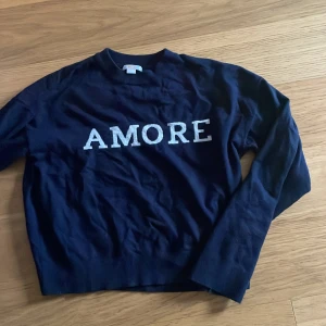Mörkblå tröja med AMORE från Gina Tricot - Mörkblå långärmad tröja från Gina Tricot med vit text 'AMORE' framtill. Klassisk rund halsringning och rak passform. Perfekt för dig som vill ha en enkel men snygg statementtröja.