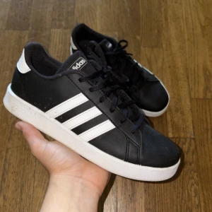 Svarta Adidas sneakers med vita ränder - De tvättas innan dem fraktas! Snygga svarta Adidas sneakers med klassiska vita ränder på sidorna och vit sula. Skorna har snörning och rund tå, samt Adidas-logga på häl och plös. Ovandelen är i syntetmaterial och designen är clean och tidlös, perfekt för en streetwear-look.