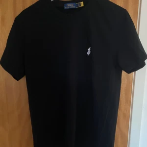 Svart t-shirt från Polo Ralph Lauren - Svart Ralph lauren T-shirt i bra skick. Har en liten defekt på märkte (sista bilden). Priset kan diskuteras vid snabb affär. Har du några fler frågor får du gärna höra av dig.