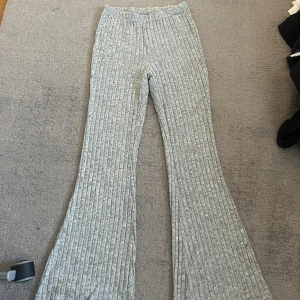 Grå ribbade bootcut byxor från SHEIN - Grå ribbade byxor från SHEIN i mjukt stickat material. Byxorna har bootcut-ben och elastisk midja för skön passform.Säljes i storlek S (EU 36). Kommer även med en topp (strapless).