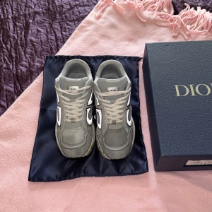 Dior b30 - Säljer ett par grå sneakers från Dior med stor vit CD-logga på sidorna. Skorna har snörning, rund tå och platt sula. Ovandelen är i mesh och syntet med coola detaljer och kontrasterande paneler. Snygg och chunky siluett som sticker ut.