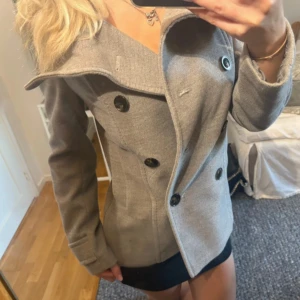 Snygg kappa - Snygg kappa med dubbelknäppning och stora svarta knappar framtill och baktill. Jackan har en bred krage och figurnära passform som ger en stilren look. Perfekt för dig som vill ha en klassisk men trendig jacka till höst och vinter.