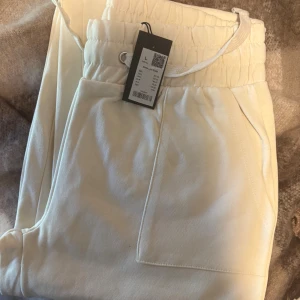 Vita mjukisbyxor med snörning - Snygga vita mjukisbyxor med bred resår i midjan och snörning. Byxorna har raka ben och praktiska sidfickor. Perfekta för en avslappnad och chill stil.