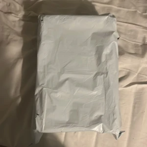 Skor  - Boken är inslagen i ett vitt plastomslag, vilket gör att varken titel eller författare är synliga. Inga detaljer om innehåll eller genre kan utläsas från bilden.