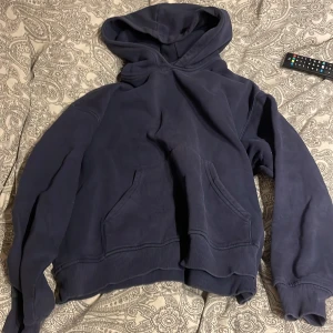 Mörkblå hoodie gina - Säljer en mörkblå hoodie med stor huva och magficka. Tröjan har ribbade muddar vid ärmslut och nederkant, perfekt för chill dagar. Passformen är loose och materialet känns mjukt och skönt mot huden.