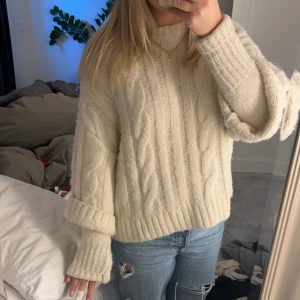Beige stickad kabeltröja - Mysig beige stickad tröja med kabelstickat mönster och ribbade muddar. Tröjan har en lite loose passform och långa ärmar som kan vikas upp. Perfekt för kyliga dagar. Den har inbyggda ärmar. Tröjan är från Zara.