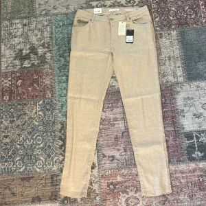 Beiga linnebyxor från Hansen & Jacob - Snygga beiga linnebyxor från Hansen & Jacob med klassisk femficksdesign och bälteshällor. Byxorna har en rak passform och är tillverkade i en stretchig linnemix som ger en avslappnad men stilren look. Perfekta för dig som gillar en ljus och fräsch stil.