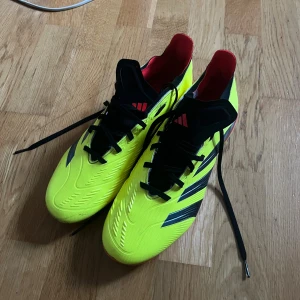 Adidas Predator fotbollsskor gul/svart - Säljer ett par Adidas Predator fotbollsskor i neon-gult med svarta och röda detaljer. Skorna har klassisk snörning, låg profil och mönstrad ovandel i syntetmaterial för extra grepp. Perfekta för dig som vill sticka ut på planen.