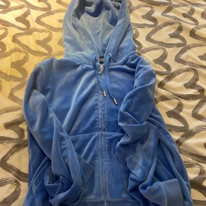 Blå velour hoodie med dragkedja - Mjuk och skön blå hoodie i velour med huva och snörning. Tröjan har dragkedja framtill och kängurufickor, perfekt för en chill och avslappnad stil.