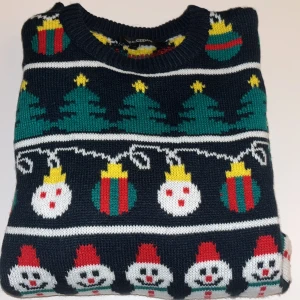 Jultröja med snögubbar från KappAhl - Mörkblå stickad jultröja från KappAhl med färgglada mönster av snögubbar, julgranar och julkulor i rött, grönt, vitt och gult. Tröjan har rund hals och långa ärmar, perfekt för att maxa julkänslan. Använd en gång, några få timmar 