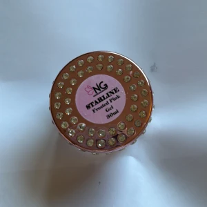 NG Starline Frosted Pink Gel - Säljer en lyxig burk med NG Starline Frosted Pink Gel, 30 ml. Burken är dekorerad med glittriga stenar och har en rosa etikett. Perfekt för att skapa snygga och glansiga naglar med en frostad rosa finish. FINNS JÄTTE LITE KVAR!! Lite mer än botten och tydligt använd men perfekt för att testa Elr 1-2 set naglar🤍