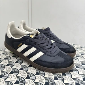 Adidas Samba sneakers marinblå - Adidas Samba sneakers i marinblått med vita detaljer och klassiska tre ränder på sidan. Ovandel i skinn och mocka, brun gummisula och snörning. Låg profil och rund tå, perfekt för dig som gillar retrostil och sportig vibe. Priset kan diskuteras 🥂