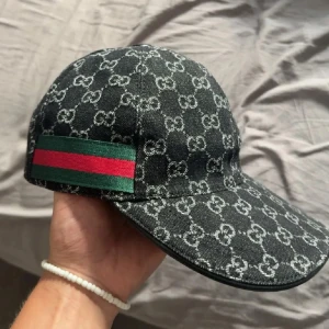 Gucci keps - Säljer en svart keps från Gucci med klassiskt GG-monogrammet. Kepsen har en grön och röd rand på sidan och justerbart spänne bak. Kommer med originalbox och dustbag. (Allt i bilderna)