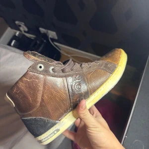 Bruna sneakers från Björn Borg - Snygga bruna sneakers från Björn Borg i skinn med detaljer i mocka och textil. Skorna har snörning, gulaktig sula och tydlig logga på sidan. Perfekta för dig som gillar en retro och sportig look med en touch av streetstyle.