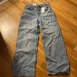 Wide ljusblå jeans från 157 - Snygga ljusblå jeans från 157 med breda ben och klassisk femficksdesign. Jeansen har en rak passform, dragkedja och knapp framtill samt råa kanter vid benslut för en cool vibe. Perfekta för dig som gillar loose och avslappnad stil.