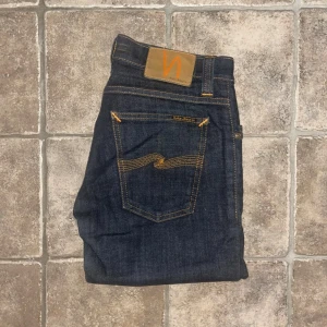 Nudie Jeans - Mörkblå jeans från Nudie Jeans med klassisk femficksdesign och kontrastsömmar i orange. Modellen är skinny och har Nudie-loggan på bakfickan. OBS modellappen saknas. Midja 36cm, längd 103cm.  Ifall det inte finns någon bild i annonsen där jag bär plaggen jag säljer så är det för att jag ej kan ha storleken heller passformen, så kolla måtten för storlek och googla på modellnamnet för passform 😉 s4