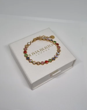 Färgglatt armband - Snyggt armband i guldton  med runda länkar dekorerade med glittrande stenar i flera färger som rött, grönt, blått, lila och vitt. Perfekt för dig som gillar färg och vill ha något som sticker ut. Justerbar längd med kedja och liten rund bricka vid låset. Lådan ingår ej.