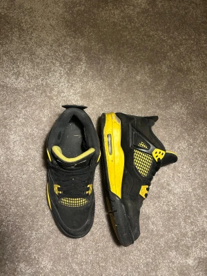 Nike Air Jordan 4 svart/gul sneakers - Nike Air Jordan 4 sneakers i svart och gul färg med klassisk meshpanel och Jordan -logga på sulan. Skorna har snörning, platt sula och detaljer i gult på sidor och undersida. Kommer med originalkartong. Perfekt för dig som gillar retro och streetwear.