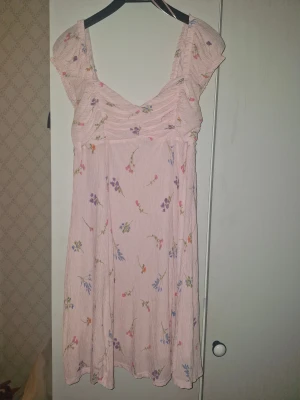 Ljusrosa blommig klänning Gina Tricot - Supersöt ljusrosa kortklänning från Gina Tricot med blommigt mönster i lila, blått, rosa och orange. Klänningen har breda axelband, lätt rynk vid bysten och en flowy passform. Perfekt för sommarens alla tillfällen!