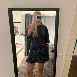 Svart blommig volangkjol New Yorker - Supersöt svart kortkjol från New Yorker med små vita blommor och volangkant. Kjolen har omlott-look med en rosett i sidan och är gjord i ett lätt och skönt polyestermaterial. Perfekt för dig som gillar trendiga och feminina detaljer. Ganska liten i storlek, jag skulle säga att det är mer som XS än S