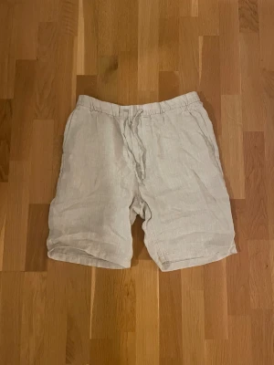 Beige linneshorts från H&M - Snygga och luftiga beige shorts från H&M i storlek M, tillverkade i linne. De har en relaxed passform, elastisk midja med snörning och fickor både fram och bak. Perfekta för varma dagar när du vill vara både chill och stilren. Aldrig använda