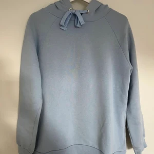 Ljusblå hoodie från Gina Tricot - Säljer en ljusblå hoodie från Gina Tricot i storlek M. Tröjan har huva med snörning och är tillverkad i mjuk bomullsmix. Långärmad modell med ribbade muddar vid ärmslut och nederkant. 