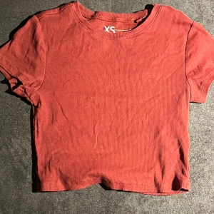 Röd ribbad croppad topp XS - Säljer en röd croppad topp i ribbad bomull med rund hals och korta ärmar. Enkel och snygg design som är lätt att matcha med jeans eller kjol. Perfekt för dig som gillar stilrena och bekväma plagg.