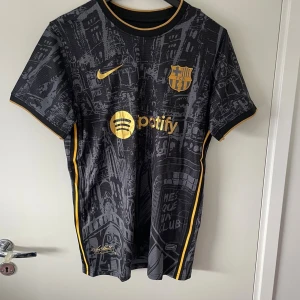 Barcelona svart matchtröja Nike - Snygg Barcelona fotbollströja i svart med guldiga detaljer och tryck från Nike. Riktig fet till sommaren eller när som.