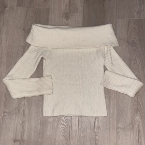 Offshoulder ribbad tröja från H&M - Säljer en vit  ribbad stickad tröja från H&M i storlek XS. Tröjan har offshoulder-design med bred krage och långa ärmar. Perfekt för dig som gillar en clean och stilren look med lite extra edge.