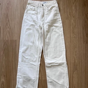 Vita jeansbyxor från NA-KD - Snygga vita jeans från NA-KD i storlek 36. Modellen är högmidjad med raka ben och har slitsdetaljer vid bensluten. Klassisk femficksdesign och tillverkade i bomull för en skön känsla. Använda ett par gånger för några år sedan. Önskar du veta exakta mått? Tveka inte att höra av dig!