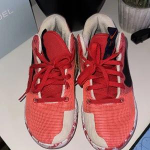 Röda Nike KD sneakers med mönstrad sula - Säljer ett par Nike KD sneakers i rött och beige med svart swoosh på sidan. Skorna har snörning och en unik rödvit mönstrad sula med KD-logga. Ovandelen är i ventilerande syntetmaterial och insidan är mjukt vadderad för extra komfort. Tyvärr var karlborren gått av men skorna funkar fortfarande utmärkt. Storlek 42