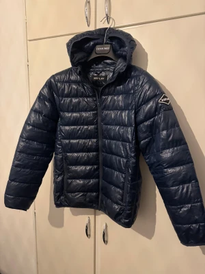 Mörkblå pufferjacka från Replay - Snygg mörkblå pufferjacka från Replay med huva och dragkedja framtill. Jackan har quiltad design och Replay-logga på ärmen. Perfekt för kyliga dagar och har två praktiska fickor med dragkedja. Modern look och skön passform.