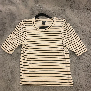 Randig topp från Lindex  - Säljer en vit och svart randig topp från Lindex i storlek XS. Toppen har rund halsringning och trekvartsärm med lätt puff vid axlarna. Materialet är mjukt.