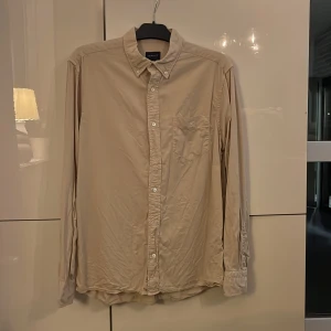 Beige skjorta från GANT Pure Prep - Snygg beige skjorta från GANT Pure Prep i regular fit. Skjortan har klassisk krage, bröstficka och knappar framtill. Tillverkad i mjuk bomull som känns skön mot huden. Perfekt för dig som gillar stilrena och enkla plagg.