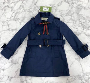 Gucci trenchcoat med bälte och rosett - Snygg trenchcoat från Gucci i grönt, marinblått och beige. Jackan har dubbelknäppning med guldknappar, bälte i midjan och detaljer vid ärmslut. Kragen pryds av en rosett med bi-emblem. Materialet är polyester och bomull, perfekt för höst och vår.2 4 6 8 10 12 years avalible