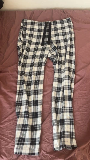 Rutig mjukisbyxa med snörning Kappahl - Snygga mjukisbyxor från Kappahl i svartvitt rutigt mönster. Modellen har normal passform, midwaist och är utrustad med svart snörning i midjan. Tillverkade i mjukt bomullsmaterial, perfekta för chill dagar hemma. Använt några få antal gånger bara, använder som pyjamas men går väl till allt möjligt. Passar mellan S/M beroende på knytning.