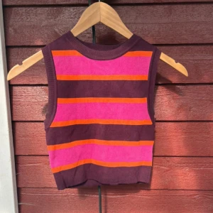 Randig ärmlös topp från Zara - Säljer en färgstark ärmlös topp från Zara med breda ränder i lila, rosa och orange. Toppen har en ribbad rund hals och croppad passform som ger en cool vibe. Perfekt för dig som gillar att sticka ut med färg och mönster.