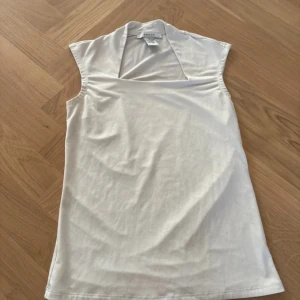 Vit ärmlös topp från Grace, XS - Snygg vit topp från Grace i storlek XS med bred krage och ärmlös design. Tillverkad i mjuk polyester och spandex som ger en skön stretchig känsla. Perfekt för dig som gillar minimalistisk stil och vill ha en clean look.