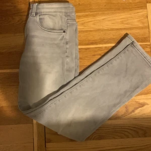 Grå jeansbyxor från Kappahl, strl 152 - Snygga grå jeansbyxor från Kappahl i storlek 152. De har klassisk femficksdesign, knapp och dragkedja fram samt raka ben. Materialet är mjukt och stretchigt för skön passform. Perfekt för dig som gillar stilrena och enkla jeans.