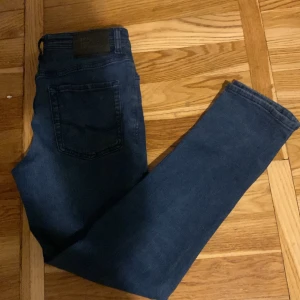 Jack & Jones Slim Glenn blå jeans - Snygga mörkblå jeans från Jack & Jones, modell Slim Glenn. Jeansen har fem fickor, smal passform och klassisk dragkedja med knapp. Materialet är stretchigt jeans och midjan är normal. Perfekta för dig som gillar stilrena och bekväma jeans.