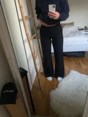 Svarta wide byxor från Lindex, strl 36 - Säljer ett par svarta byxor från Lindex i storlek 36. De är mid rise och ett snyggt wide snitt som ger en trendig siluett. Byxornas tyg påmminer lite smått om linnebyxor med klassisk dragkedja och knapp framtill. Perfekta för dig som gillar stilrena och bekväma plagg.