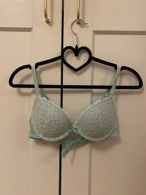 Blå blommig spets-bh från H&M - Snygg ljusblå bh från H&M med blommig spets på kuporna och justerbara axelband. Kuporna har ett tunt lager vaddering och spetsen är i polyester. Baksidan är slät och har hakknäppning. Perfekt för dig som gillar söta detaljer och pastellfärger.💕
