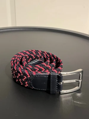 Flätat bälte 105 cm  - Flätat rött och blått mönstrat bälte. Det är 105 cm långt, men går att stretcha ut. Använt någon enstaka gång. 