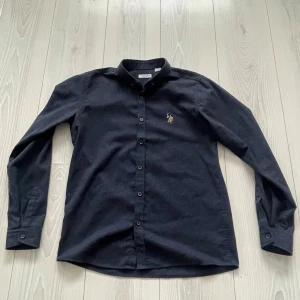 Mörkblå skjorta från U.S. Polo Assn. - Svart skjorta från U.S. Polo Assn. med klassisk krage och knappar hela vägen. Broderad logga med polospelare på bröstet. Skjortan är långärmad och tillverkad i mjuk bomull, Storlek XS/S! Skicka vid intresse. 